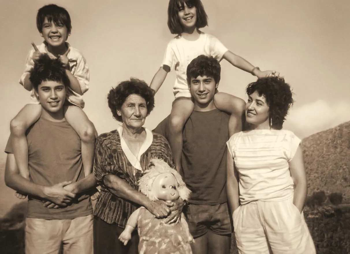 Foto antigua: una abuela rodeada de sus nietos, dos de ellos subidos a los hombros de sus hermanos